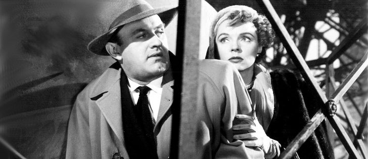 A man in a fedora and suit and tie looks sideways toward a woman, looking unsure