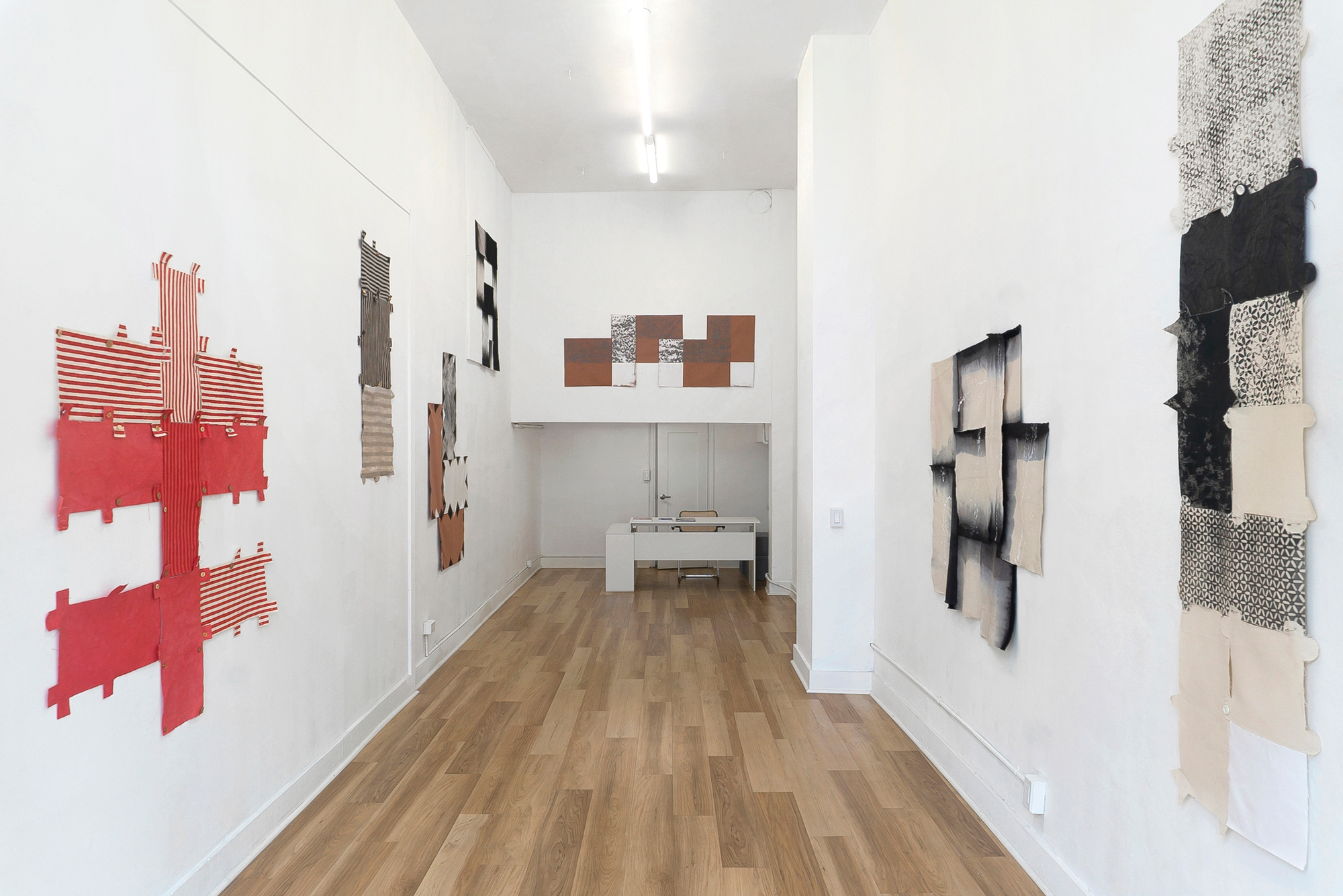 gallery view with textile works hung on walls in rectangular arrangments