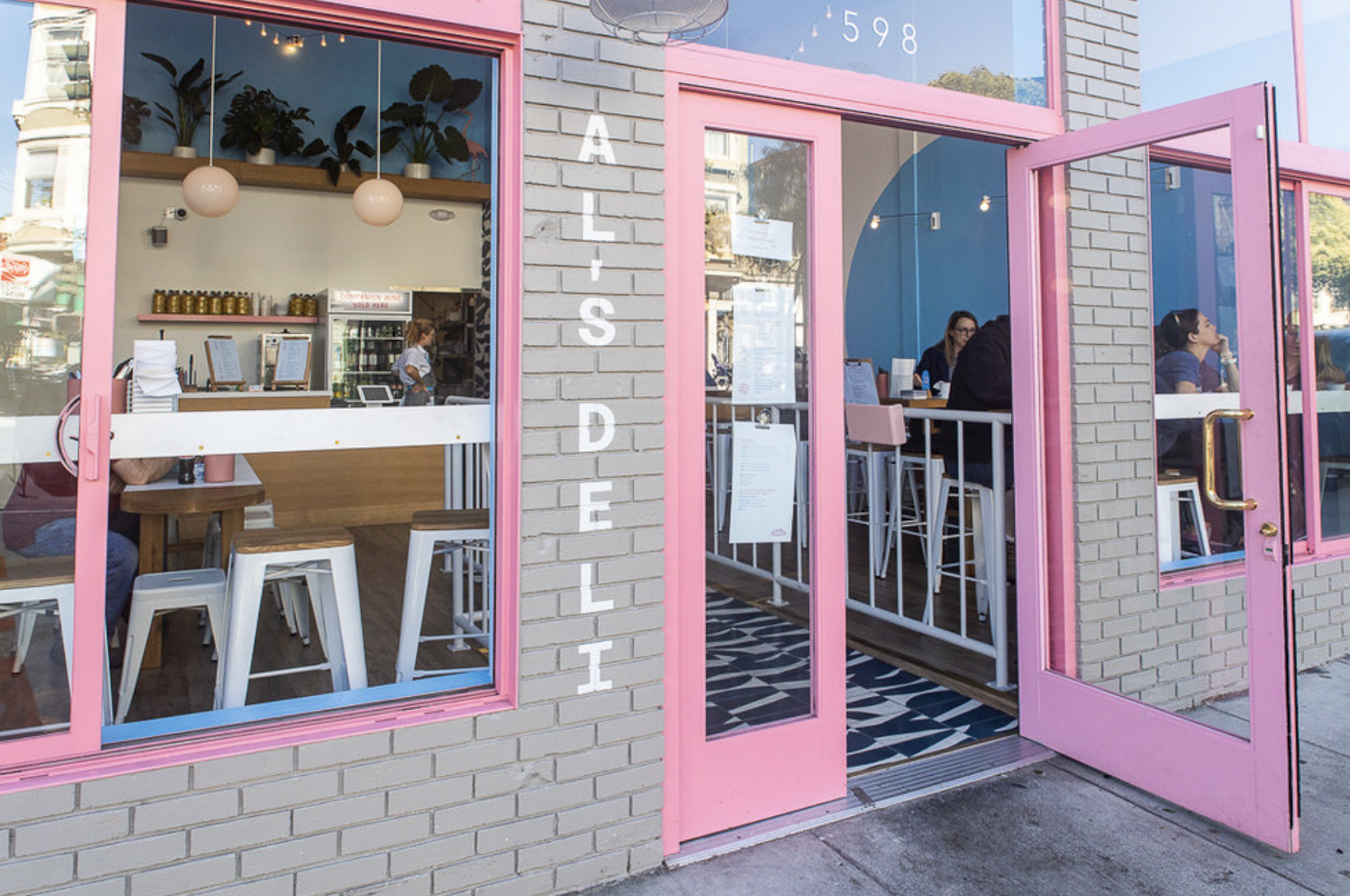 A grey brick building with large windows trimmed in pink. The front door to the restaurant is propped open.