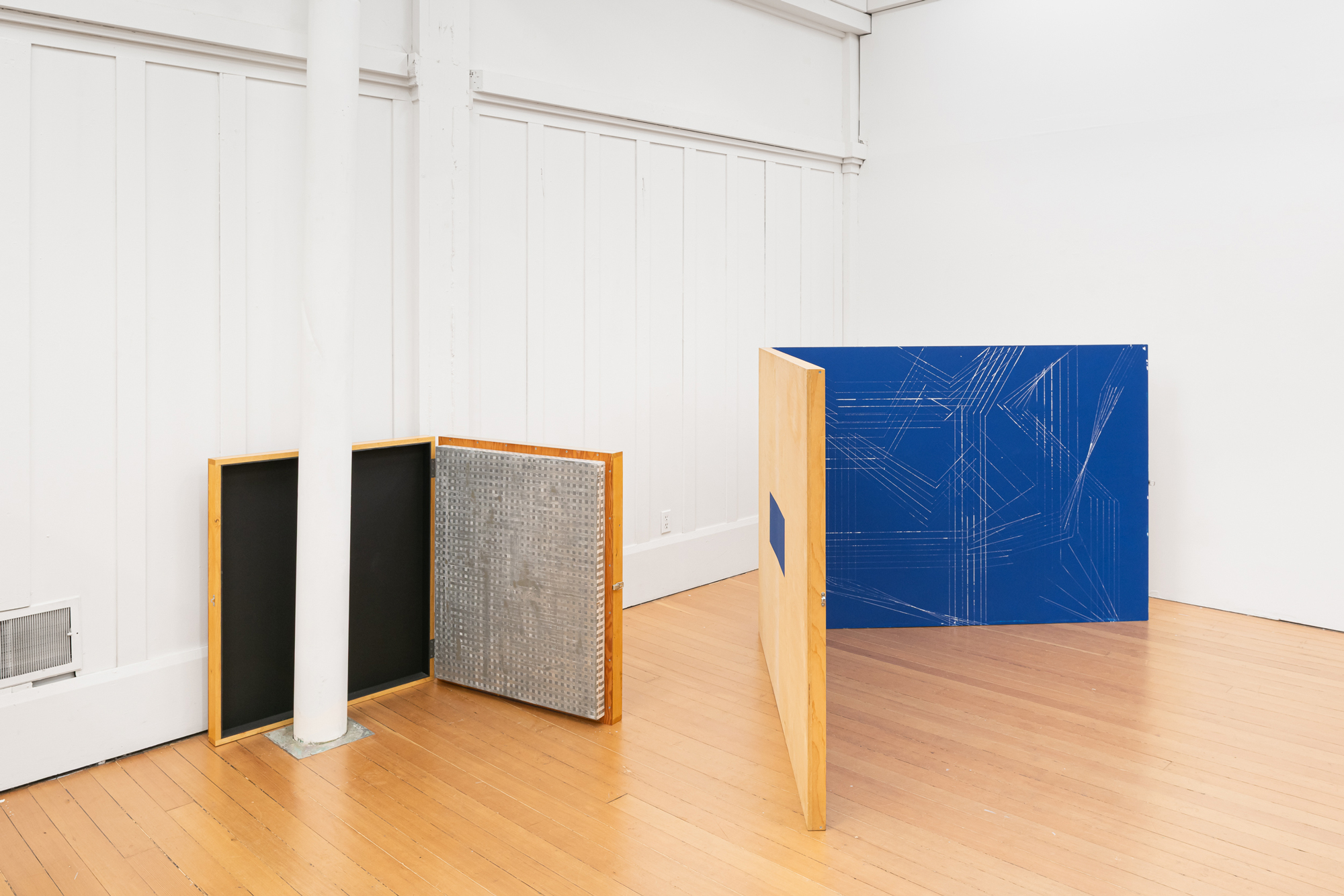 two hinged wooden painted sculptures in gallery, one behind column