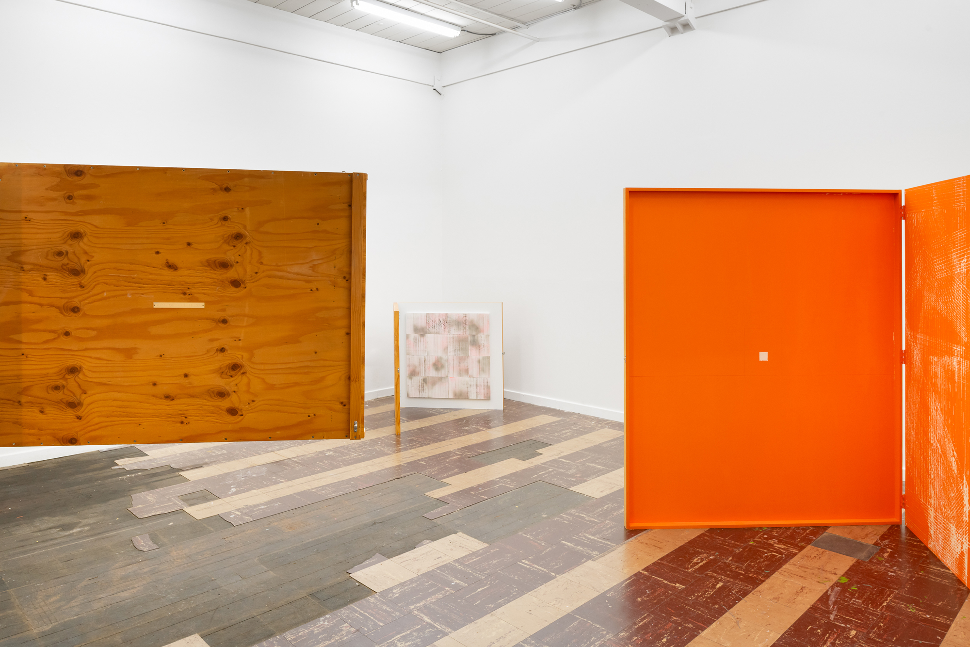 gallery view with wooden flap at left and large orange-painted hinged sculpture at right