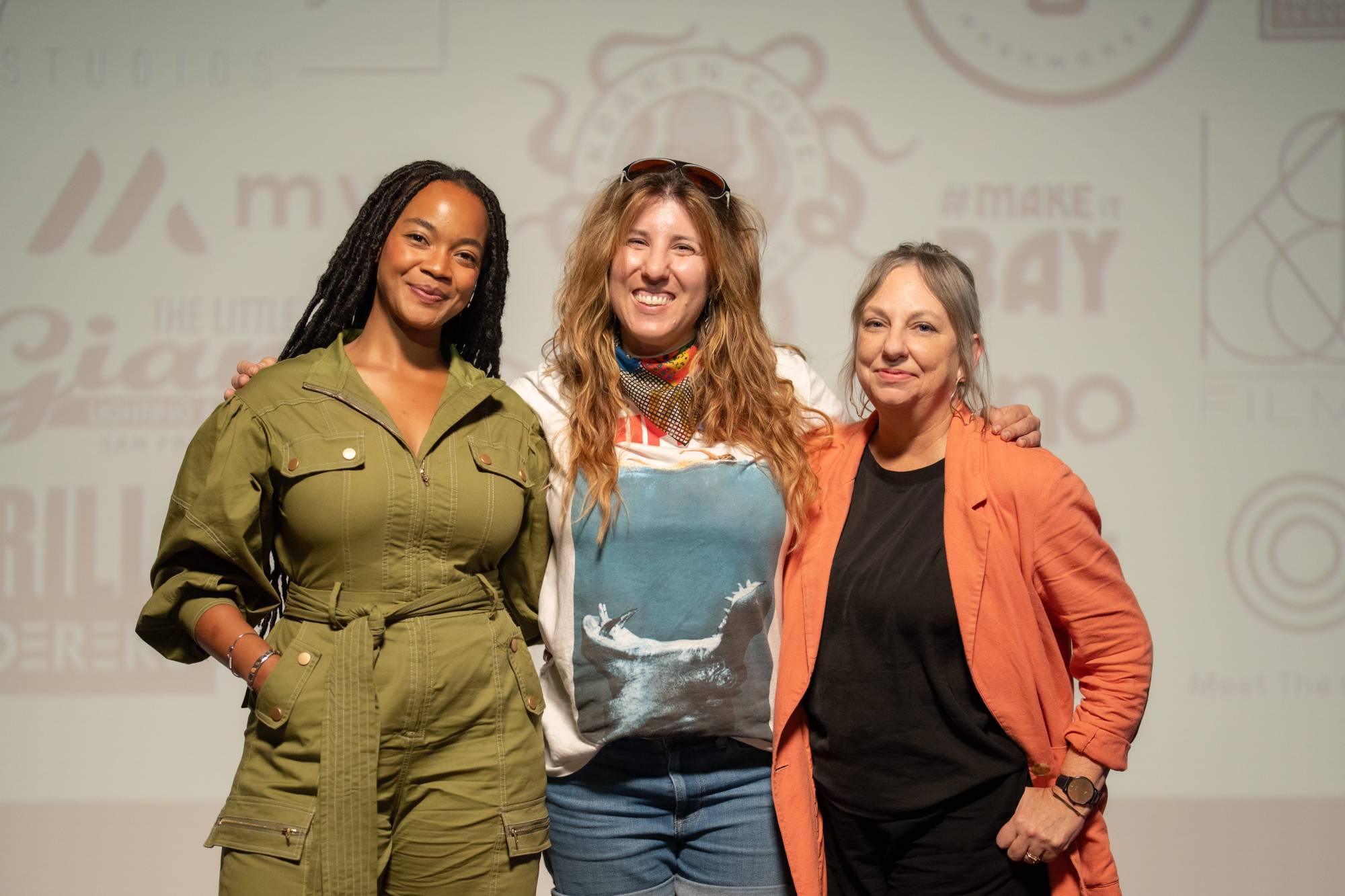 Three women stand next to each other, locked arms, posing for a photo.