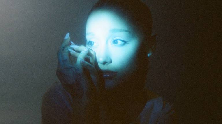 a young woman holds her hand before her face in the dark with a light blue spotlight across her eyes