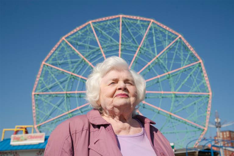 older white woman poses with ferris wheel behind her, head at center