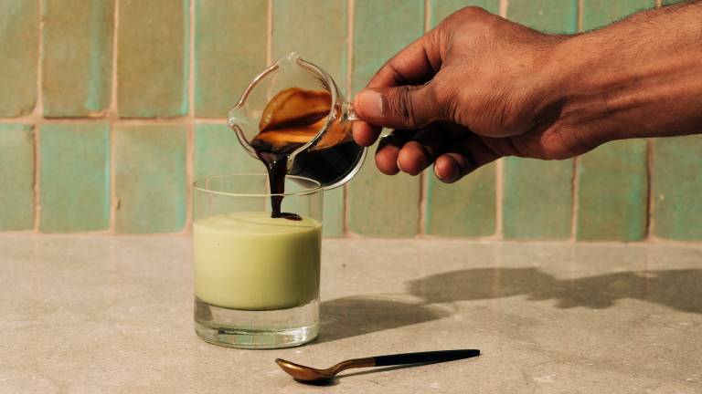 A hand pouring espresso into a blended avocado drink.