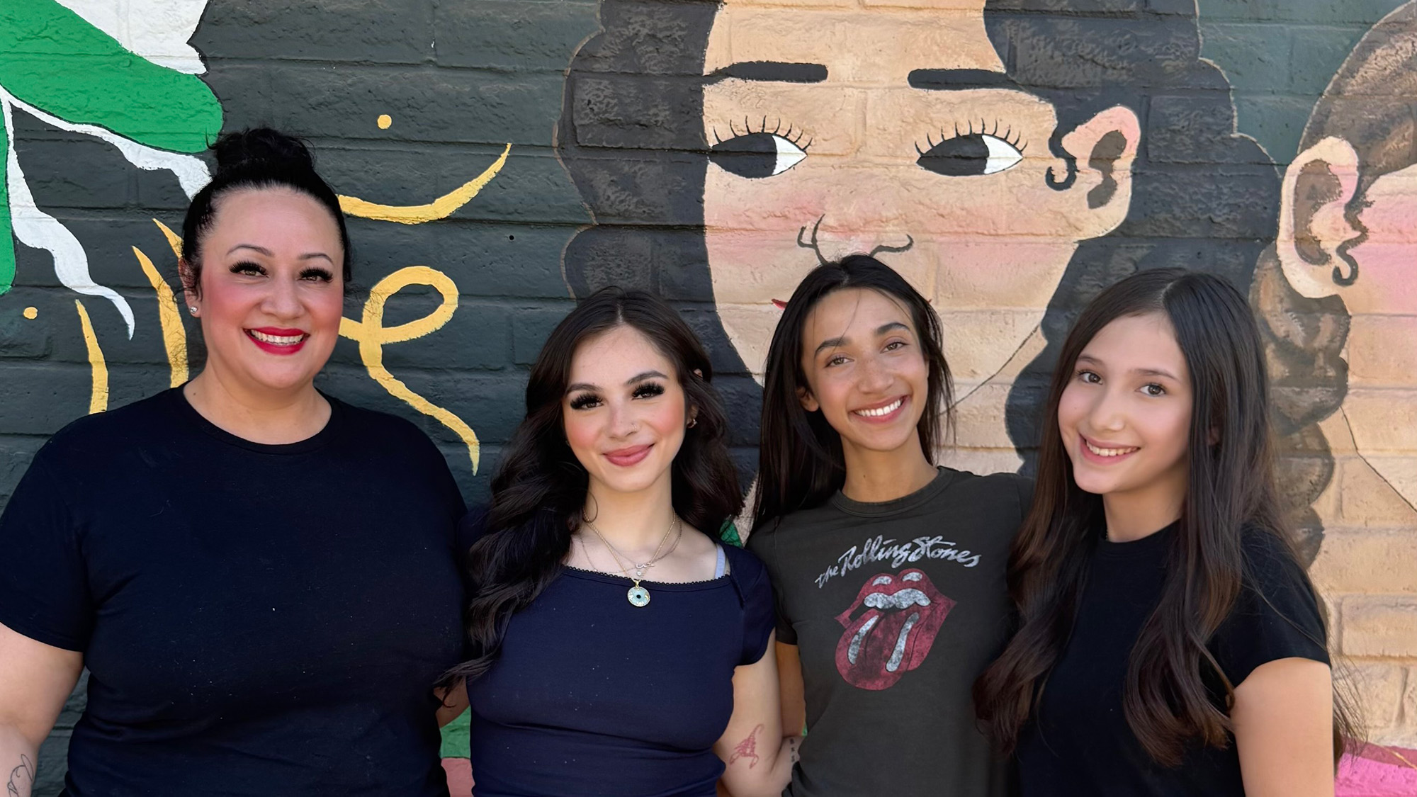 Four women pose for a portrait in front of a mural.