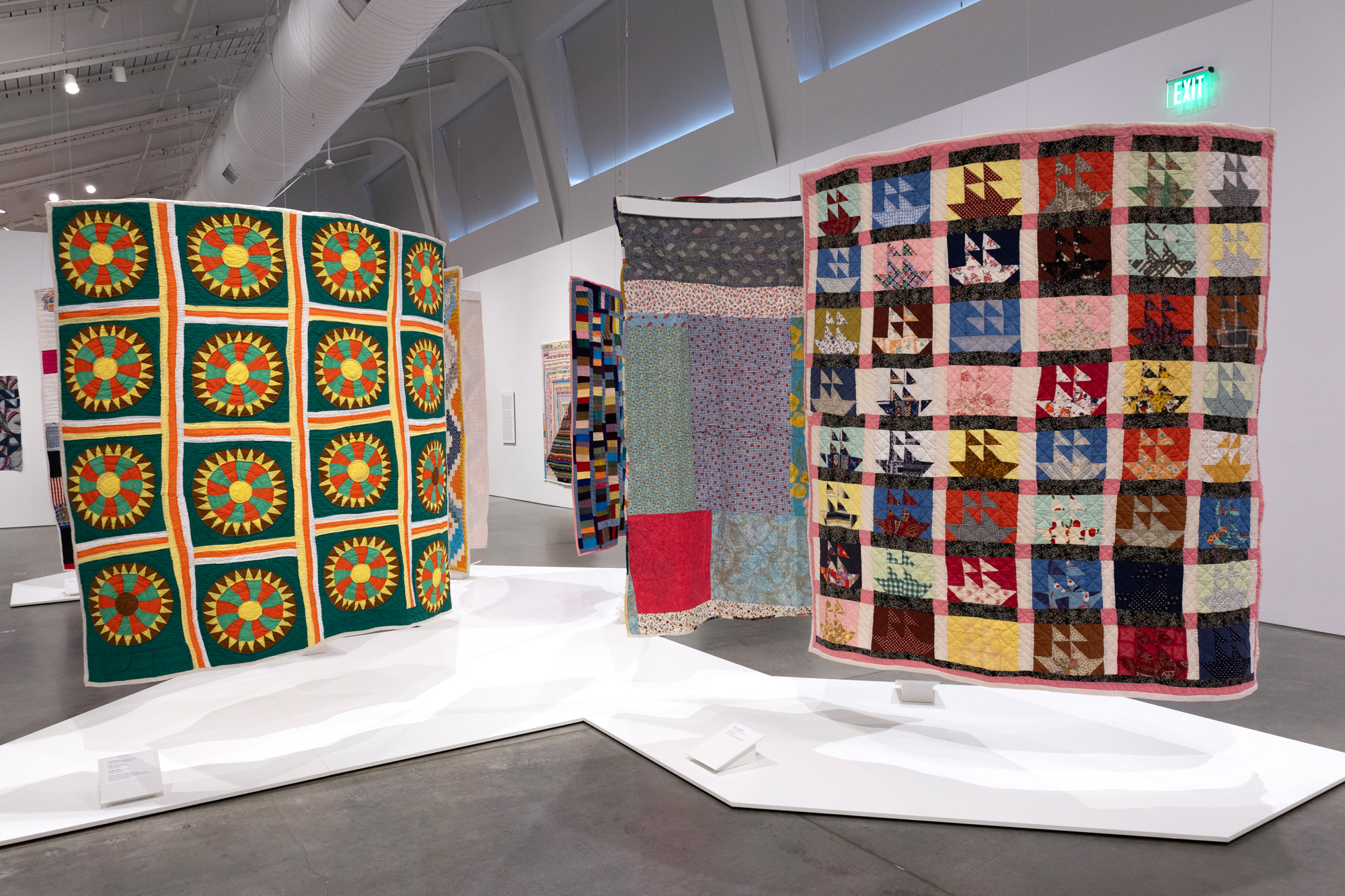 large colorful quilts hanging from ceiling in museum