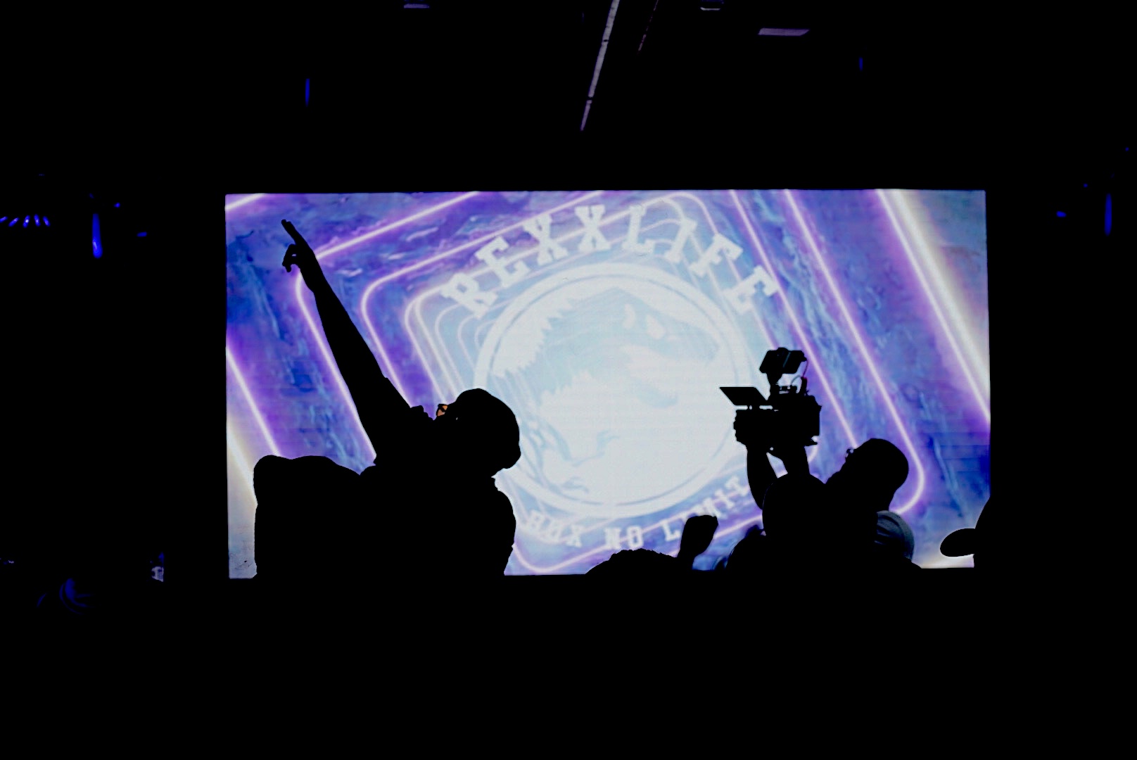 A silhouette of a man raising his right arm on stage while holding a mic with his right arm. 