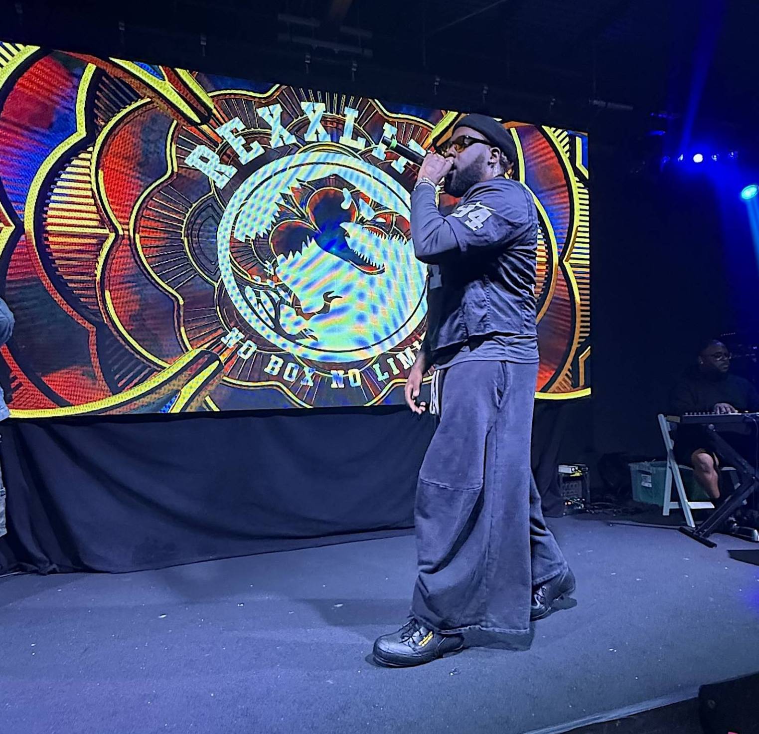 A man on stage wearing all black and sunglasses while holding a microphone.