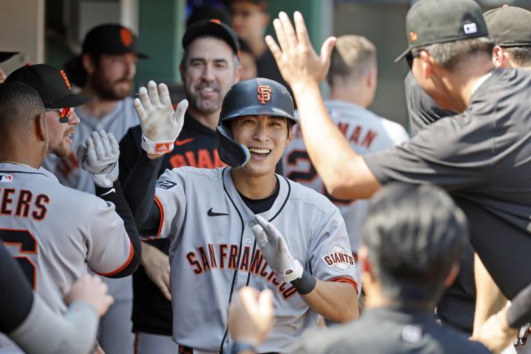 A baseball player in San Francisco uniform smiles and high fives a man wearing a black t-shirt and baseball cap.