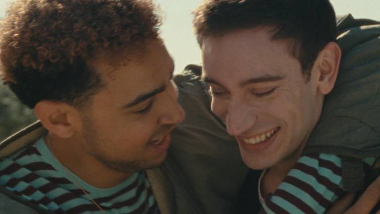 A young mixed race man playfully wraps his arm around the shoulder of a young white man who smiles in response.