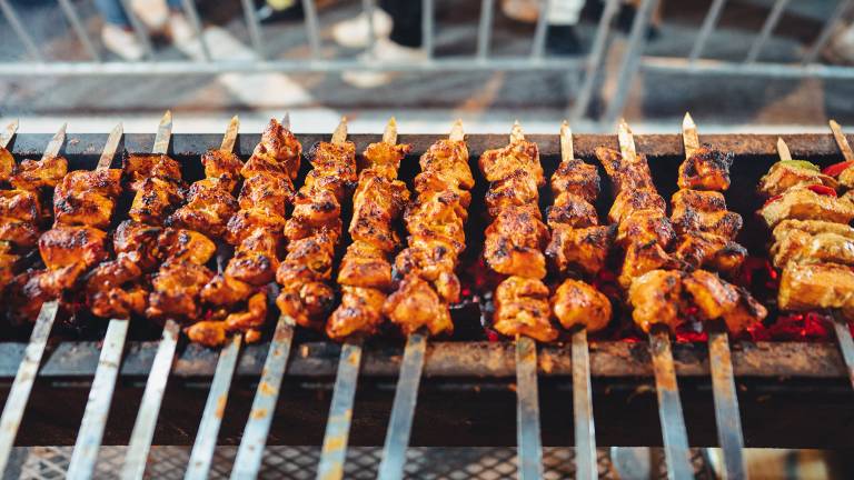 Meat kebabs on long, metal skewers cooking over a grill.