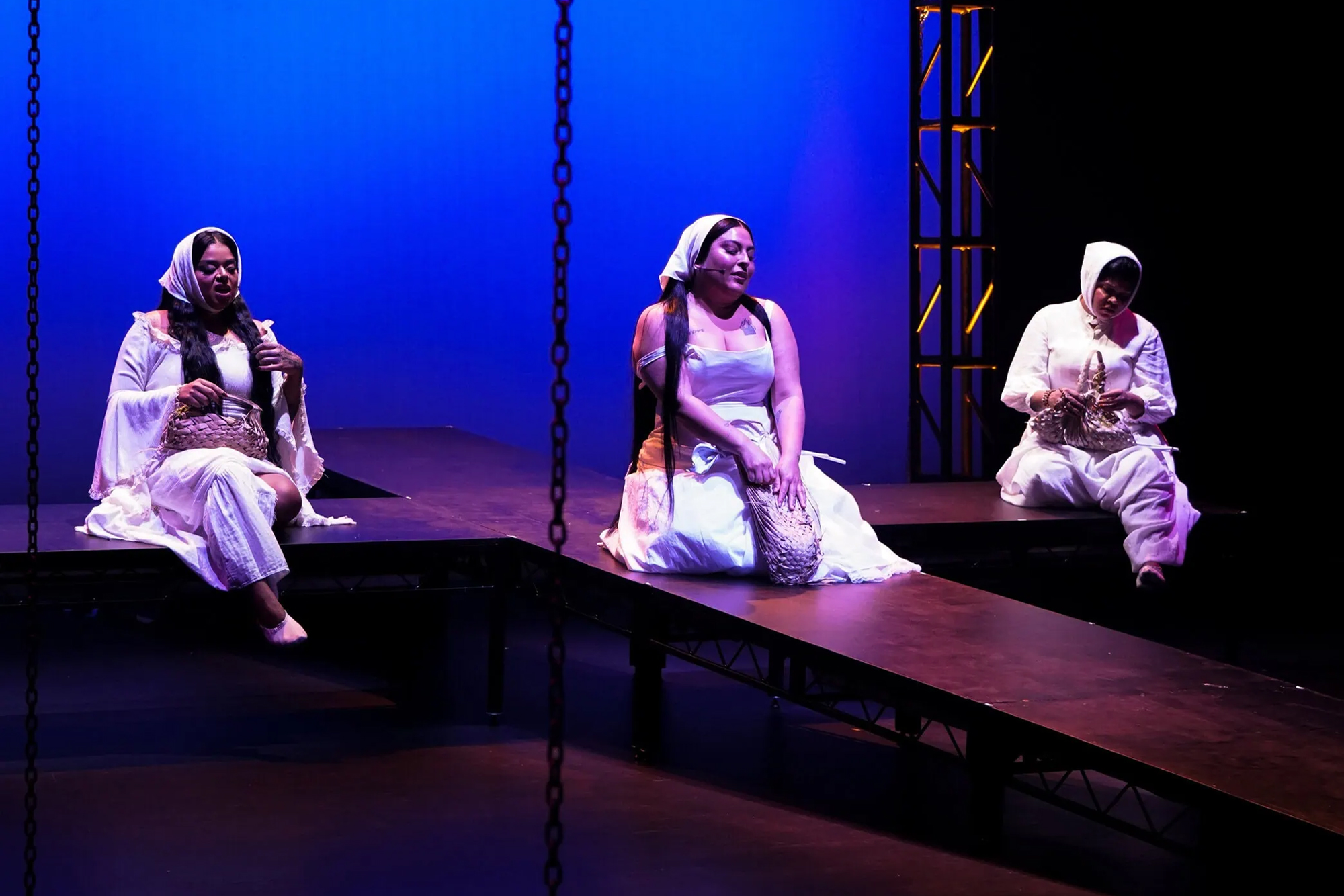 three performers in white on stage with blue background