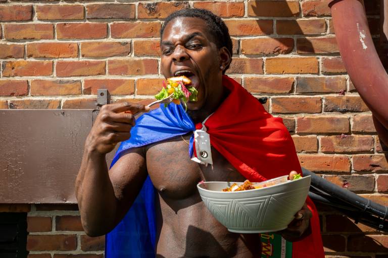 Man wearing a blue and red cap, like a superhero, eats a large forkful of salad.