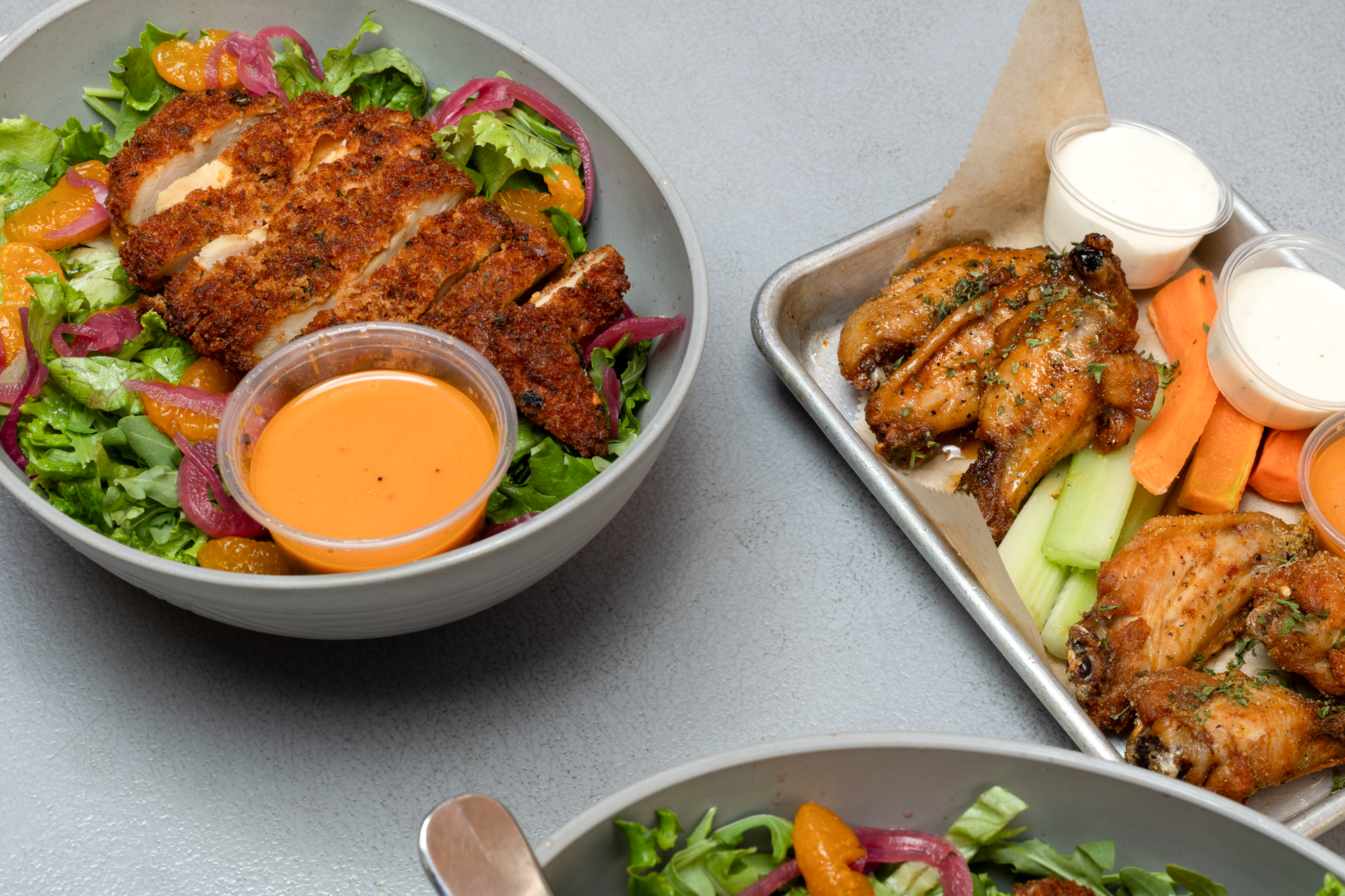 A fried chicken salad and a tray of chicken wings displayed on a counter.