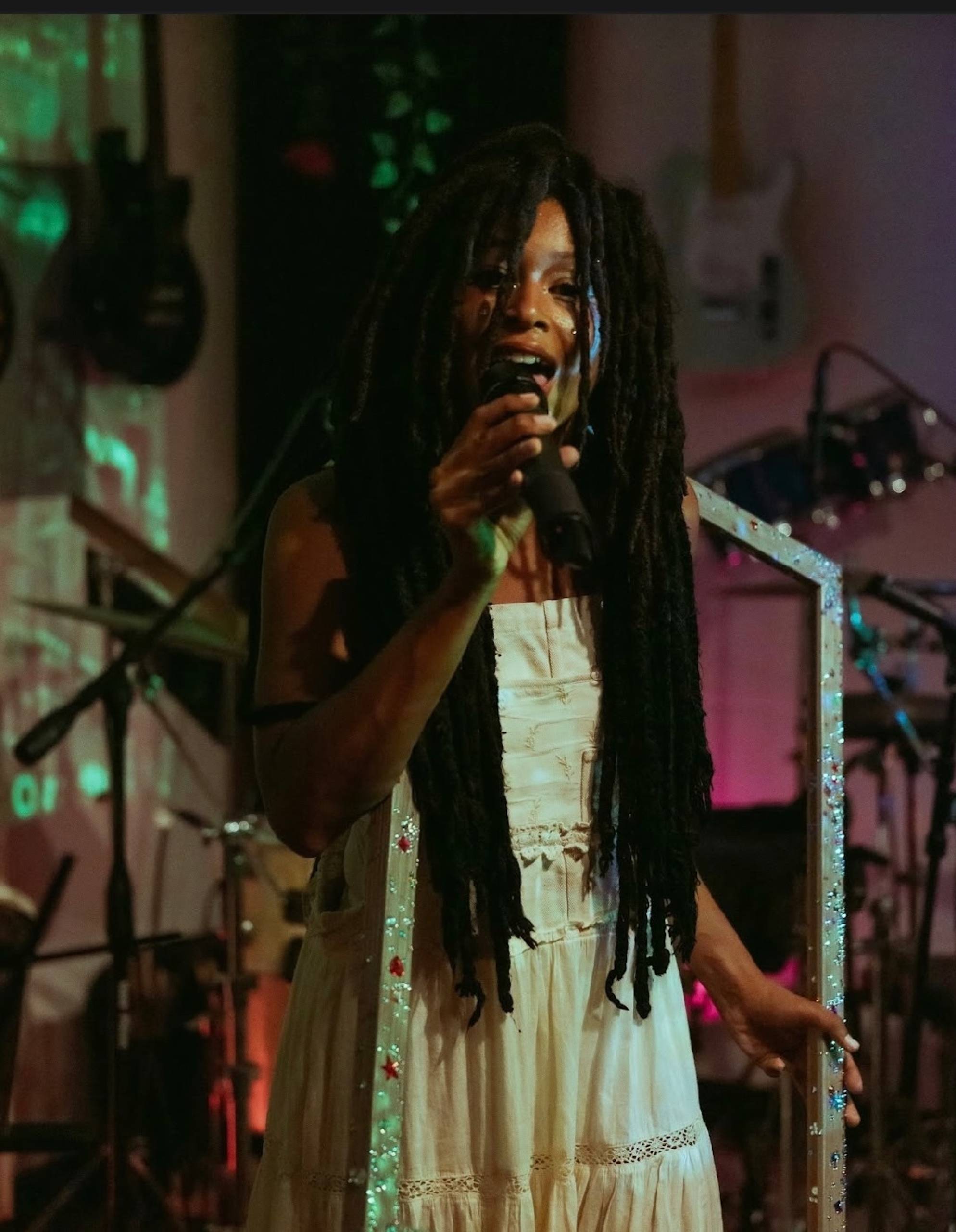 A Black woman with long locs performing on stage in a white dress. 