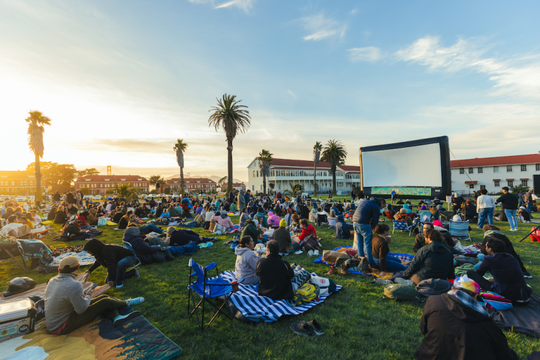 People on picnic blankets gather at a park during sunset.