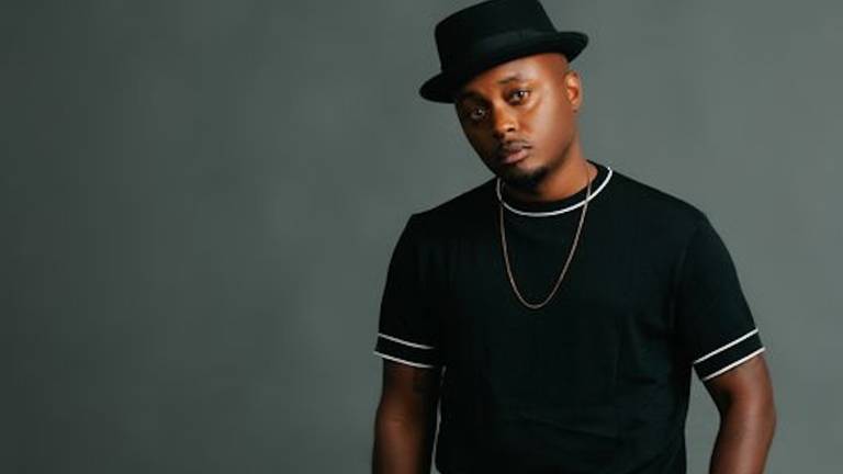 A man in a black hat, black shirt and jeans poses for a photo.