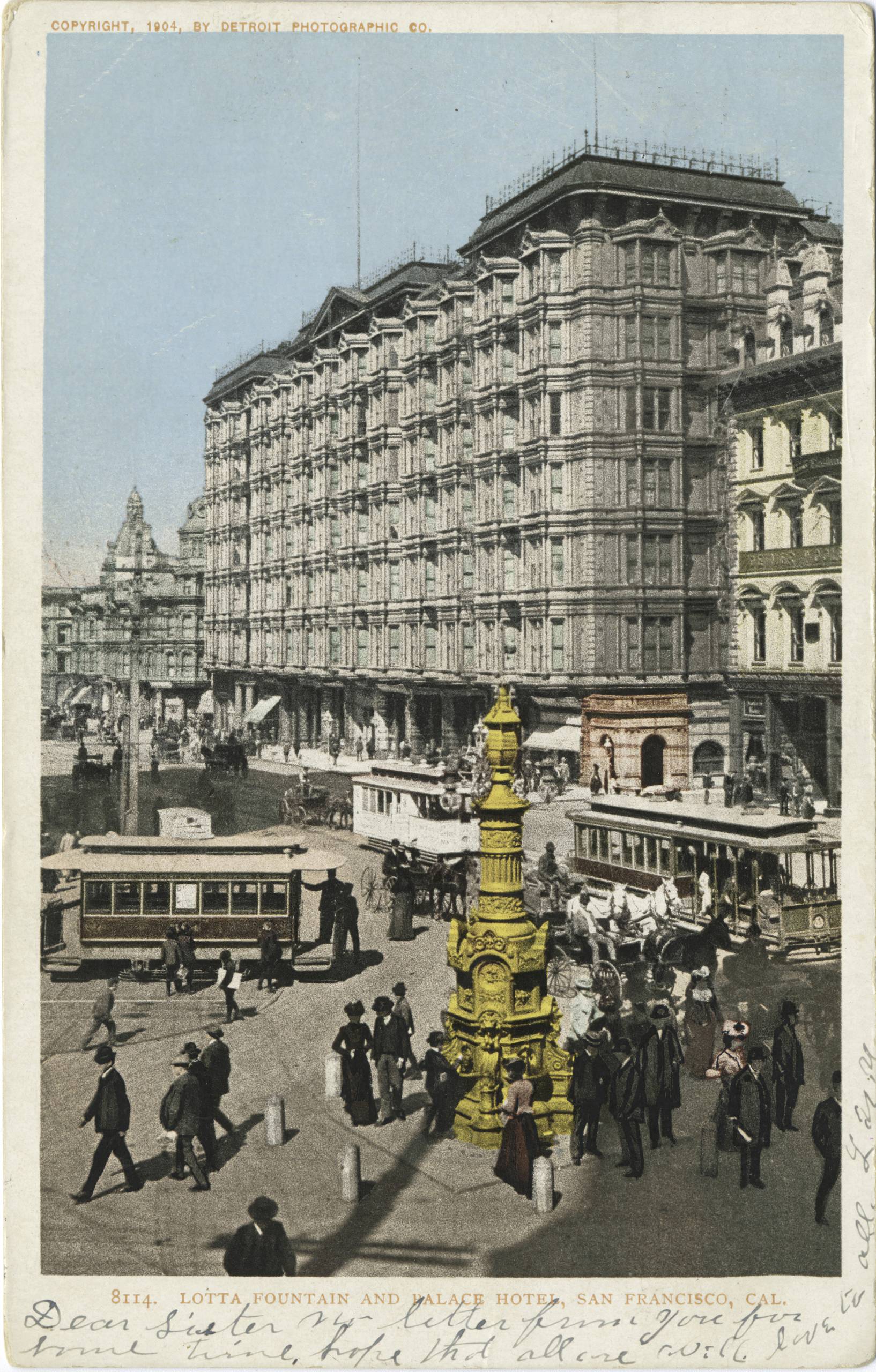 hand-tinted postcard of large hotel on busy street with yellow fountain in foreground