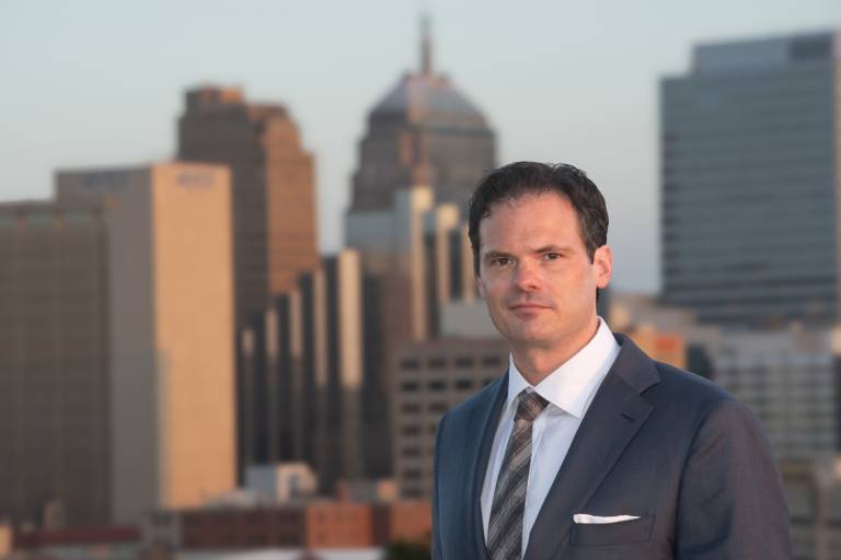 white man in suit with city skyline in background