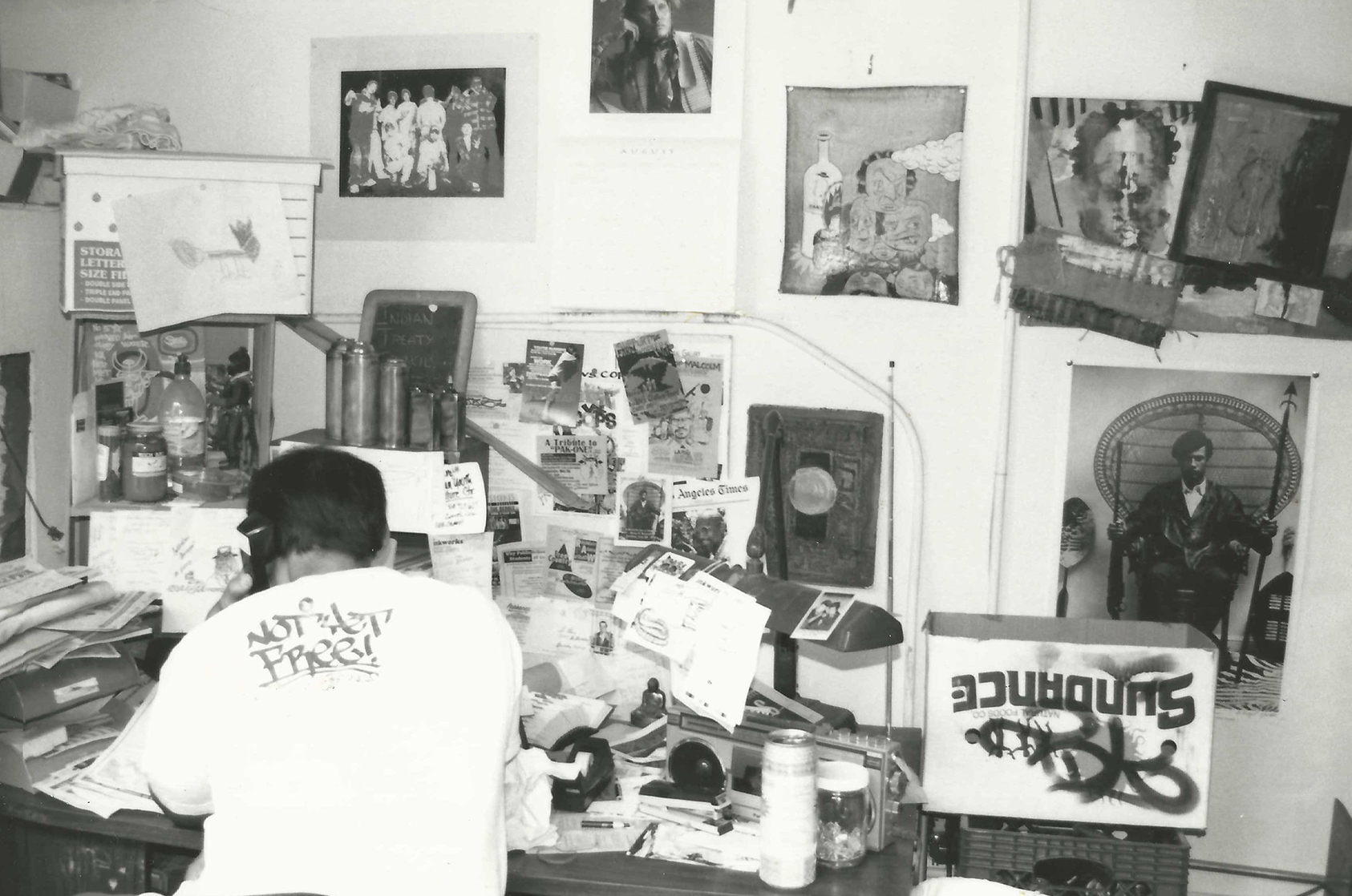 A black and white photo showing a man's back as he sits at a desk. 