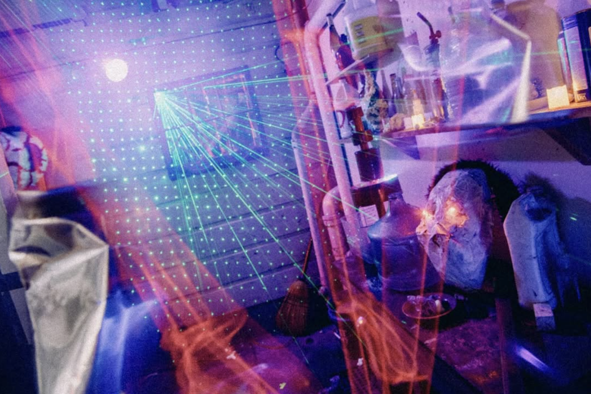 A chaotic room lit by lasers and spotlights. Bare pipes are visible on the wall. 