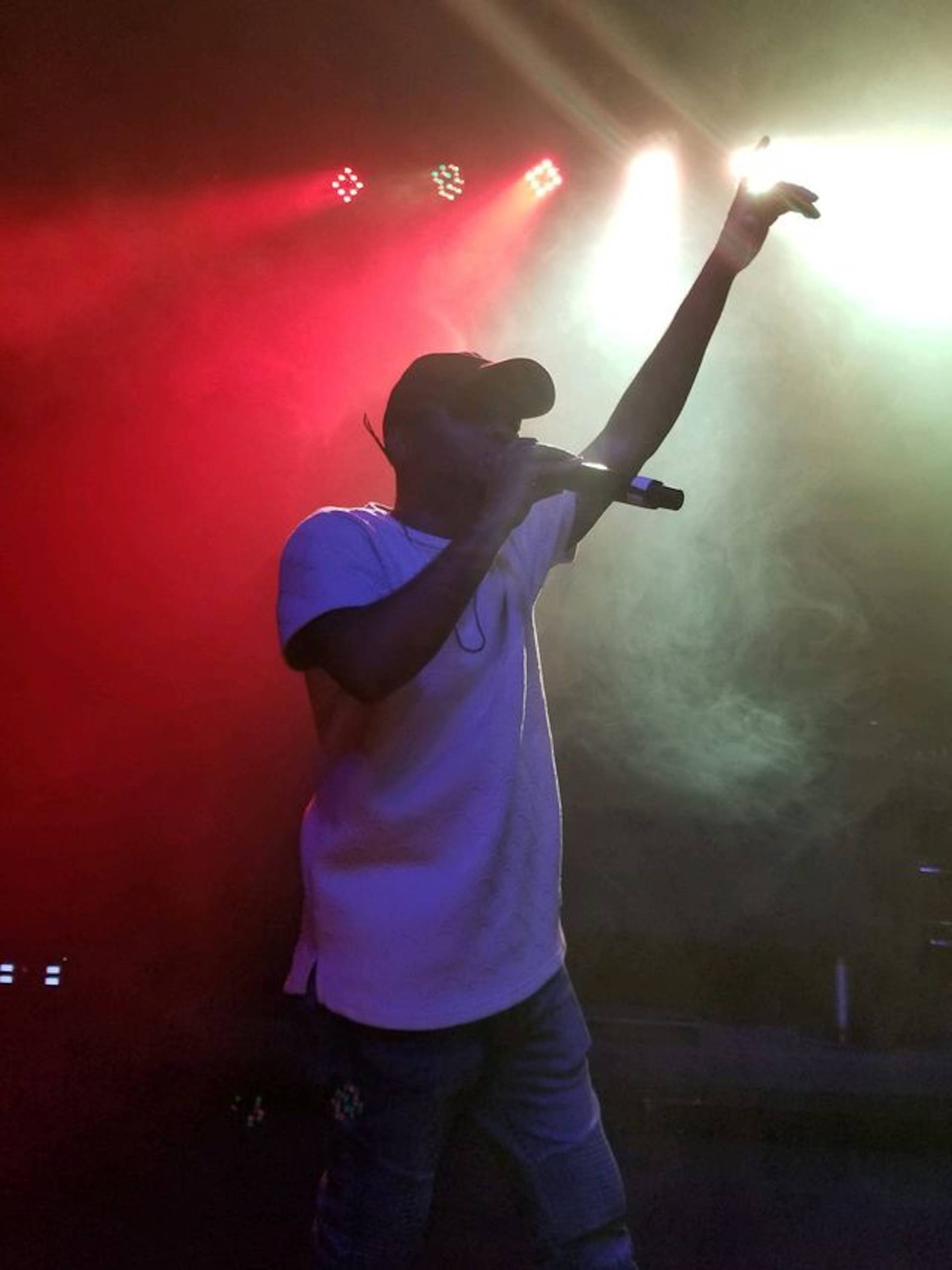 A man in a white shirt and hat, standing on stage at a smokey venue. 