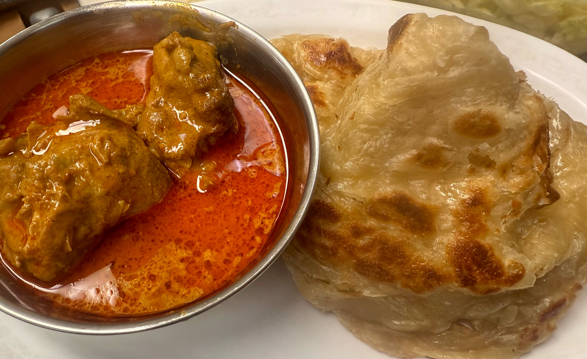 Roti flatbread with a bowl of bright orange chicken curry on the side.