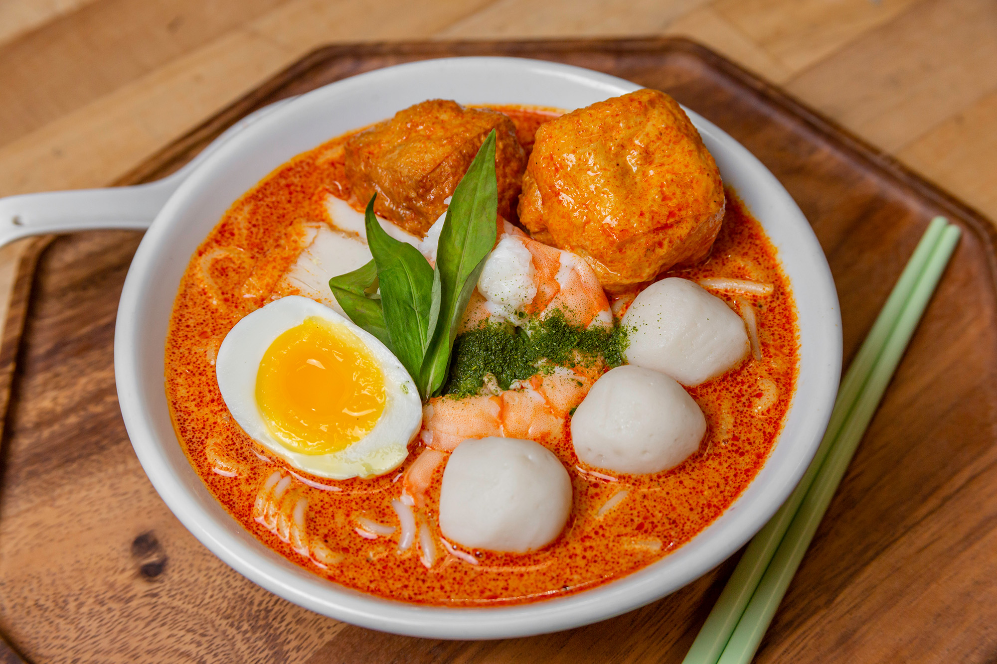 Bowl of bright orange laksa noodle soup topped with shrimp and fish balls.