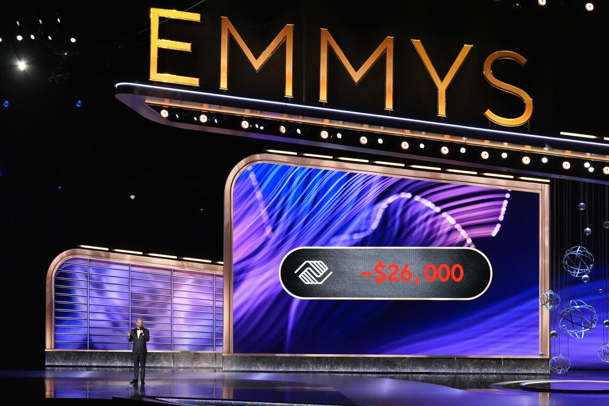 Host of Emmys awards ceremony on stage in front of a large Emmys marquee.