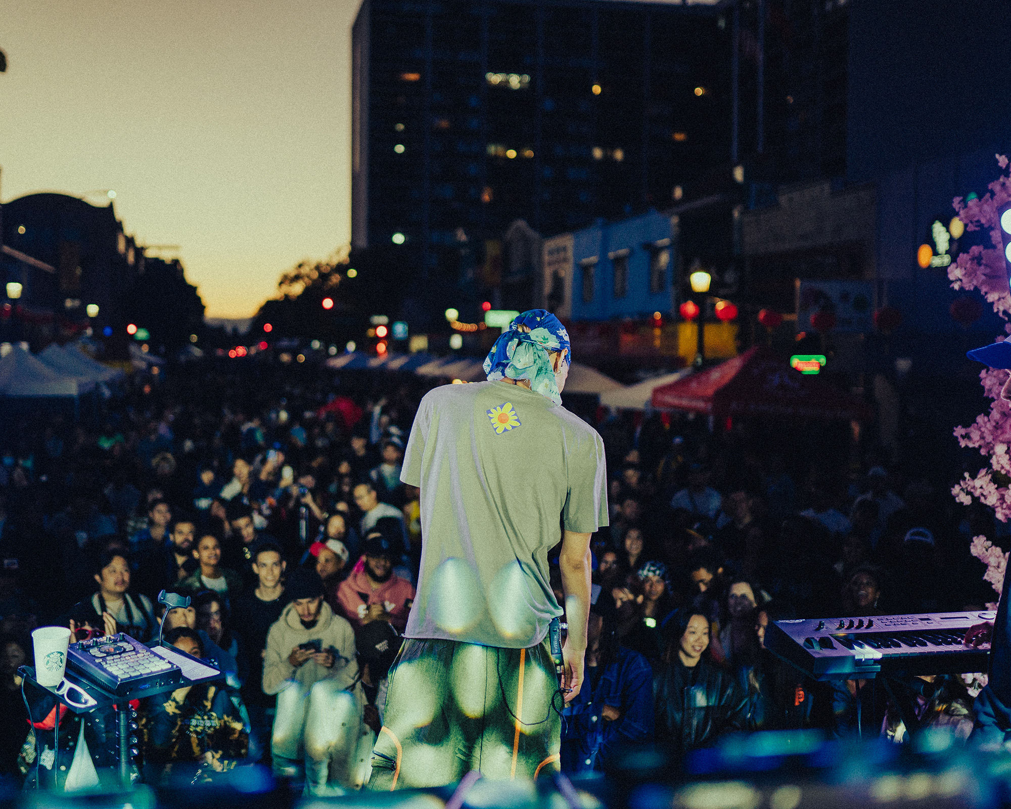 A rapper viewed from behind as he performs in front of a large crowd in the streets of Oakland.