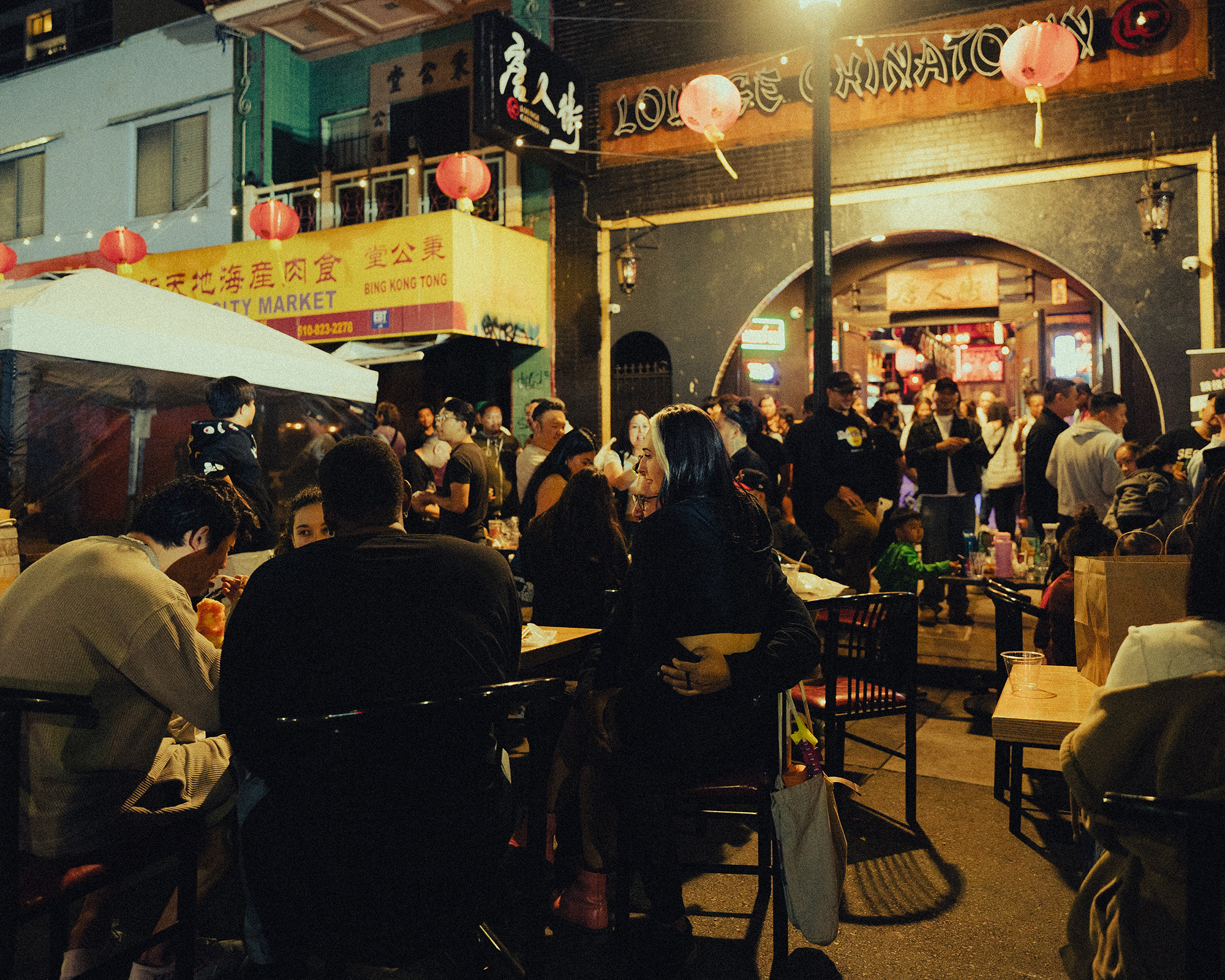 A crowd of people eating at outdoors tables in Chinatown at nighttime.