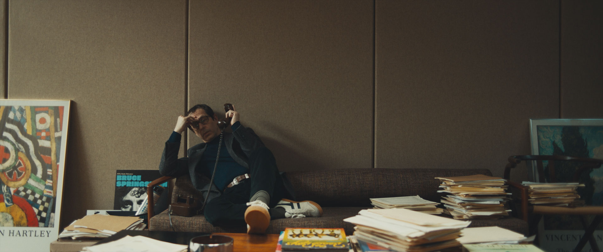 man in office with stacks of paper, on phone with head in hand