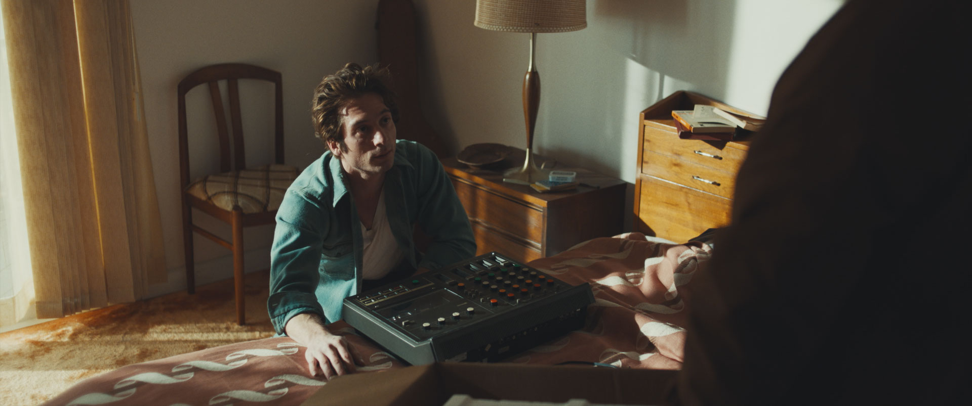 man kneels next to bed in front of recording equipment