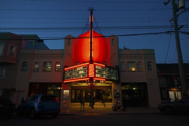 a movie theater lit up in red with a marquee about a ghost film festival