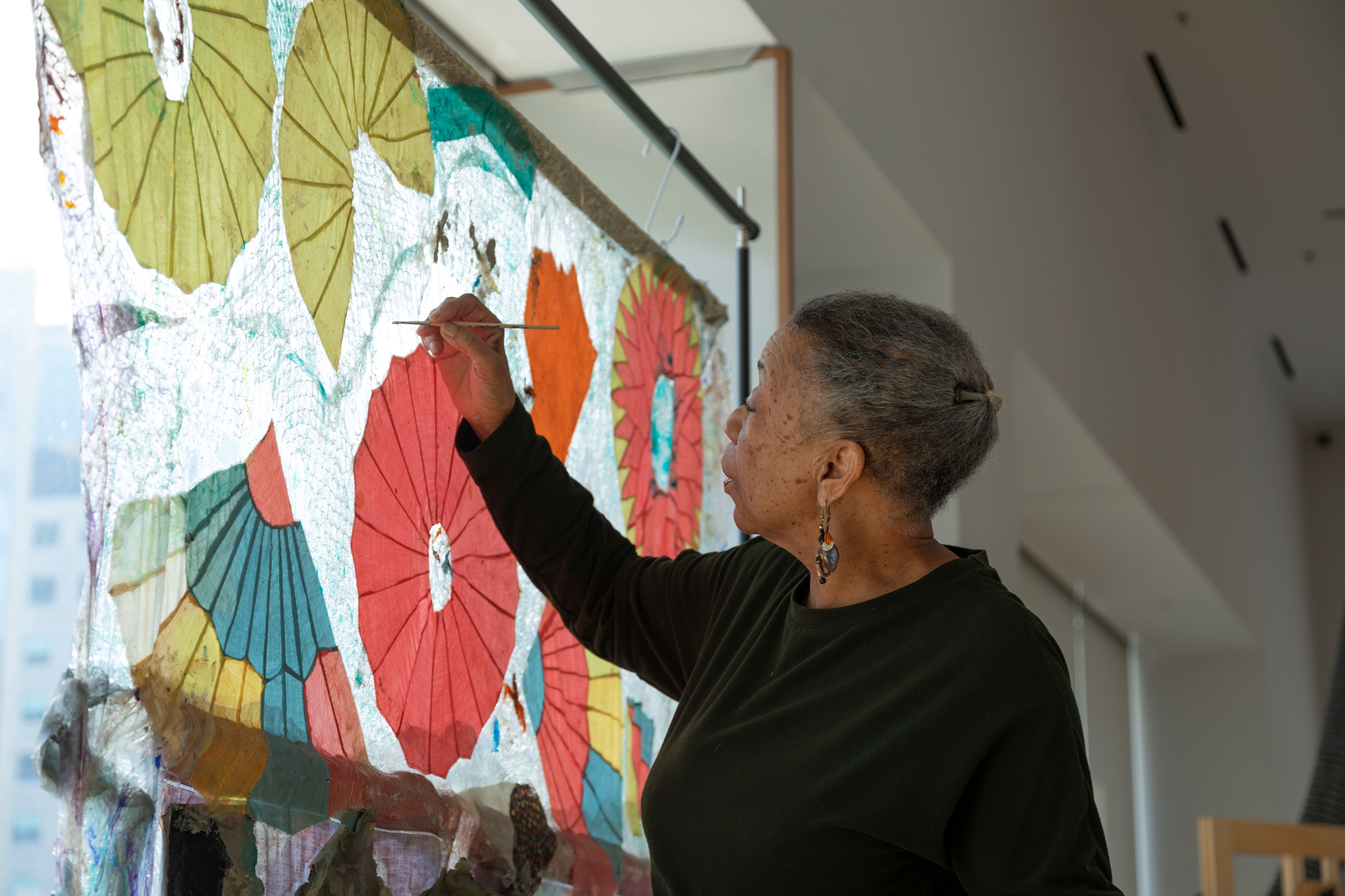 Older Black woman uses paintbrush on translucent abstract painting