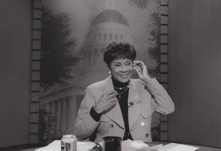 A black-and-white photo of a TV anchor adjusting her earpiece.