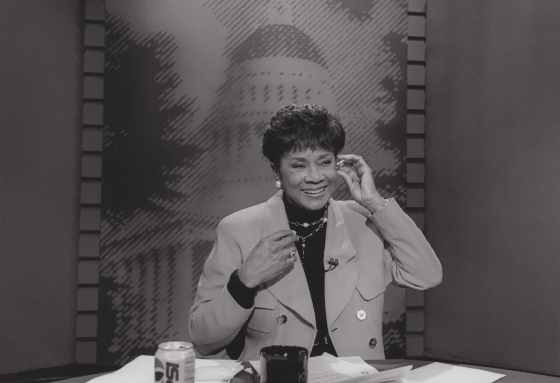 A black-and-white photo of a TV anchor adjusting her earpiece.