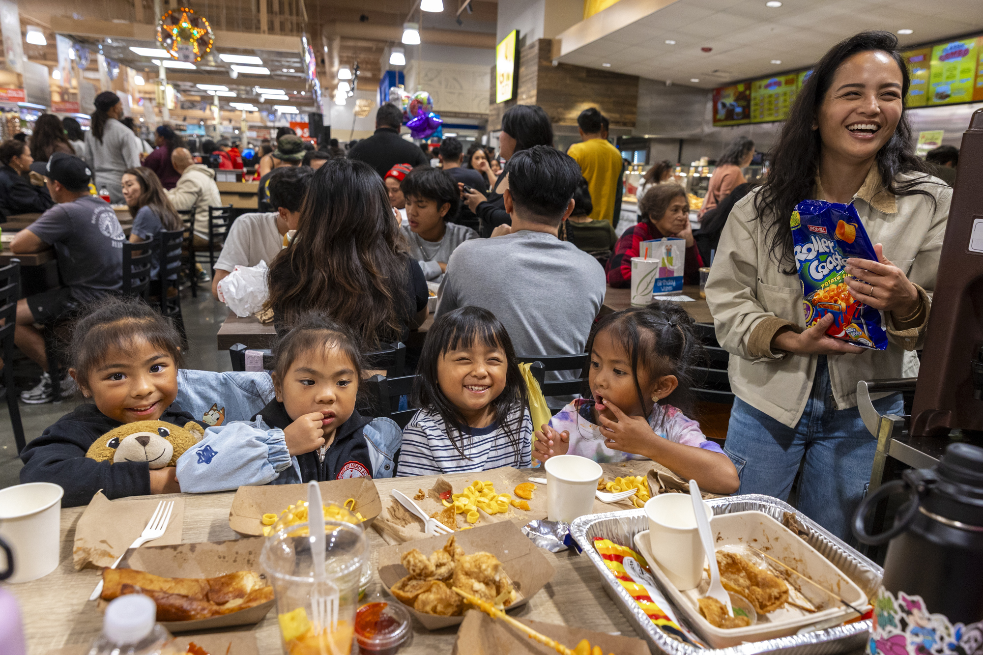 Four young children eating a spread of Filipino street food in a supermarket food court.