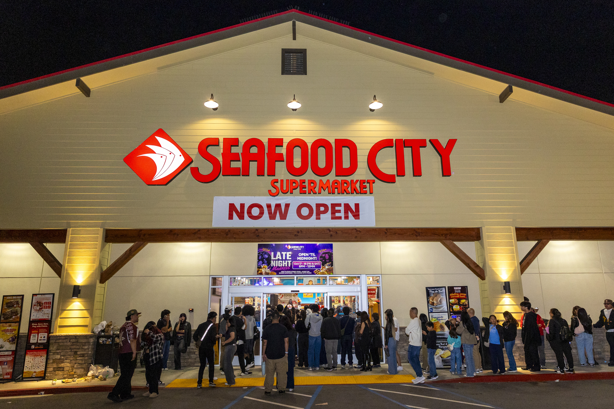 A crowd lined up outside a Seafood City supermarket at nighttime.
