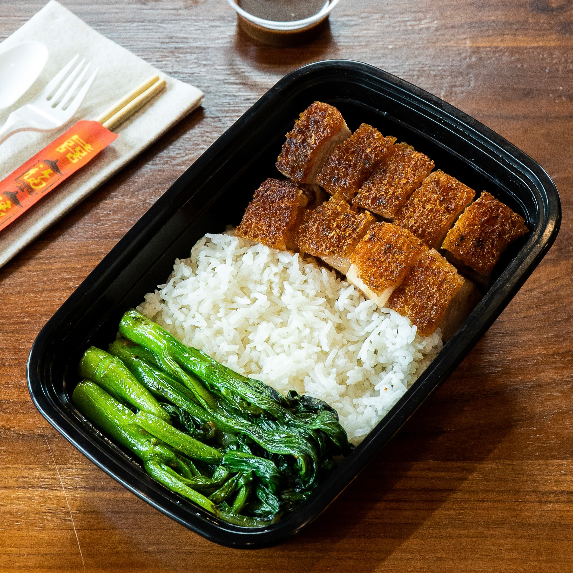 A plate of crispy roast pork belly, cut into slics and packed in a to-go container.