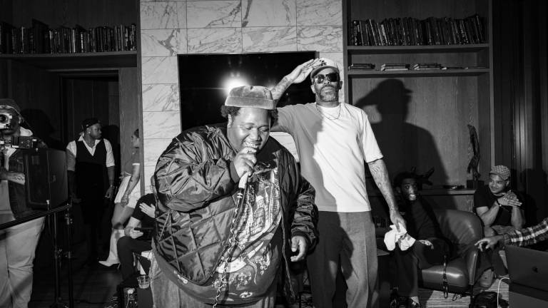 A black and white image of a man holding a microphone while performing as another man stands to his left and slightly behind him, saluting.