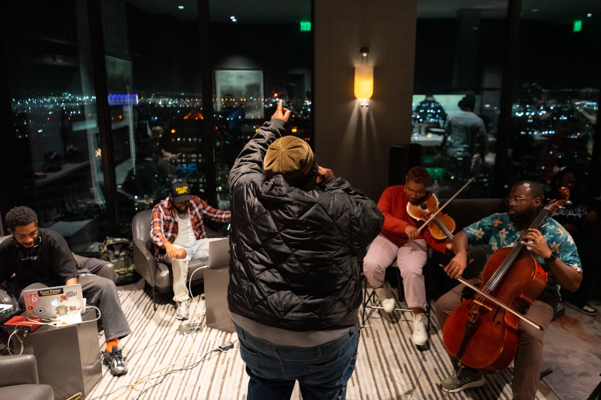 The back of man performing as a band sits around him, all of them overlooking downtown Oakland. 