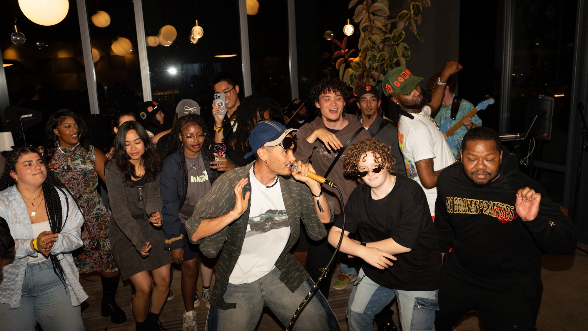 A man with a hat holds a microphone while performing in front of a lively audience. 