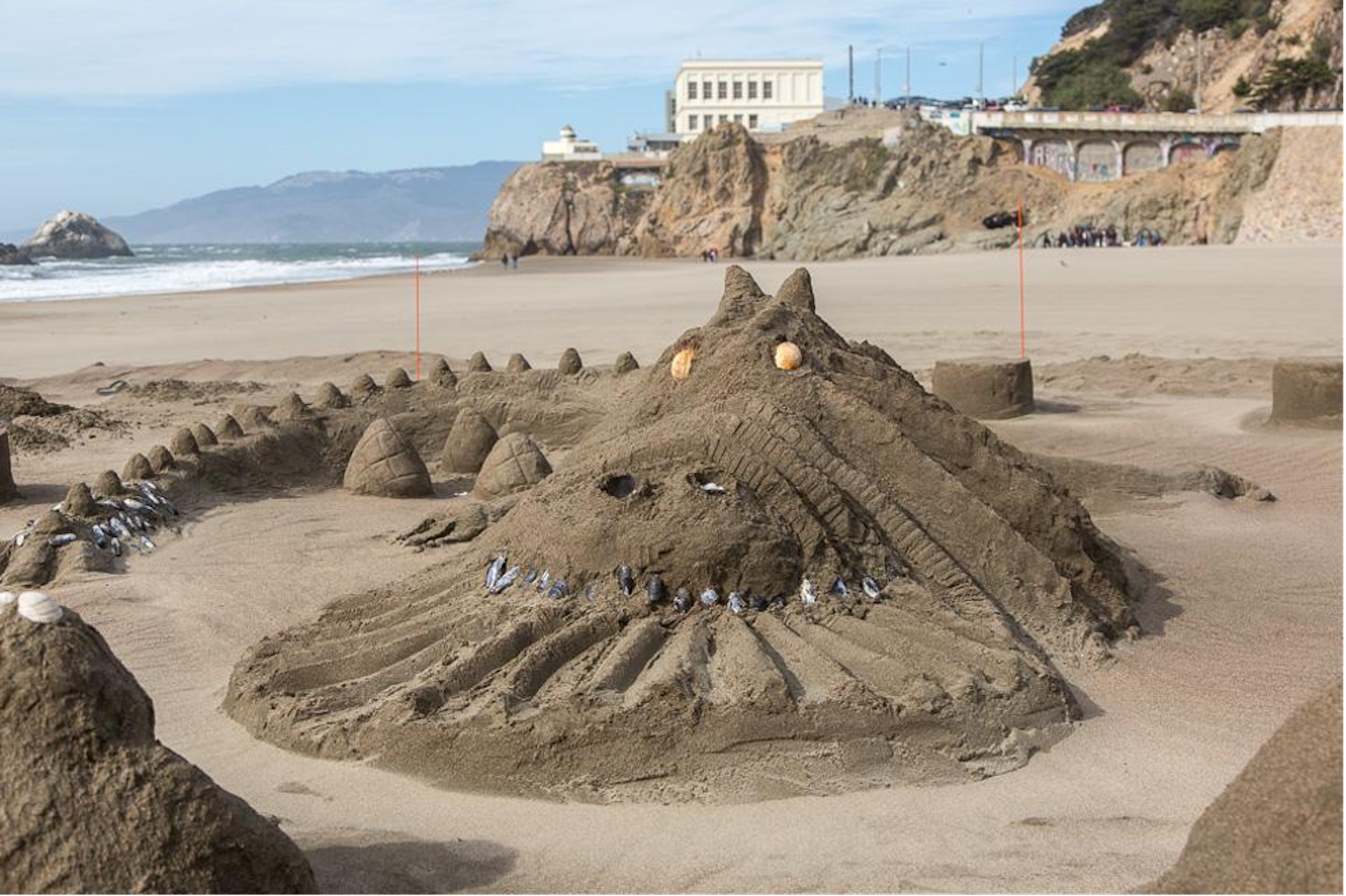 A large scale fire-breathing dragon built from sand. San Francisco's Cliff House is visible in the distance.
