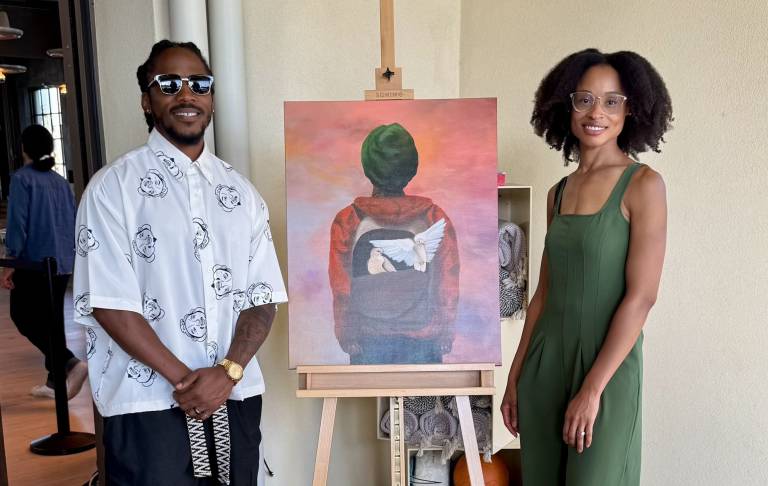 two people stand on either side of an easel with a painting, smiling