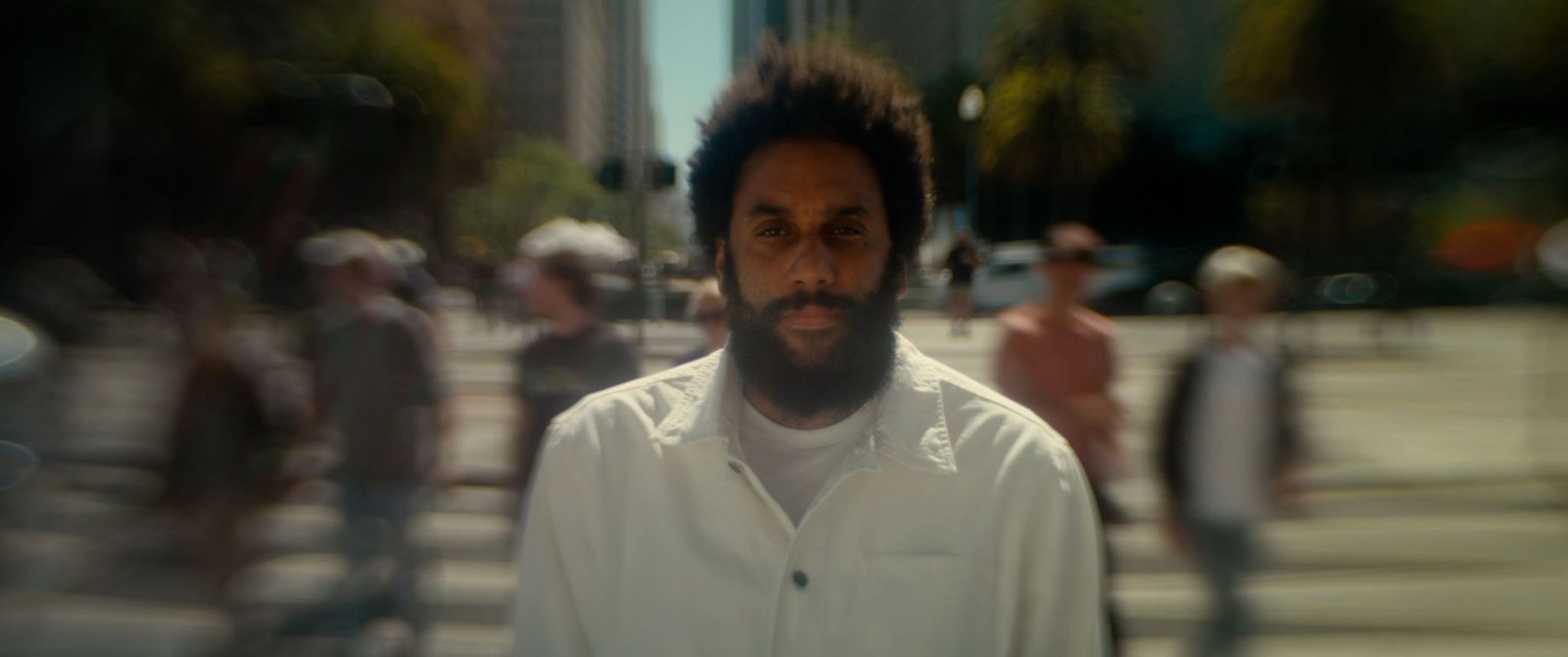 A blurry portrait of a man in a white shirt walking down the street on a sunny day.
