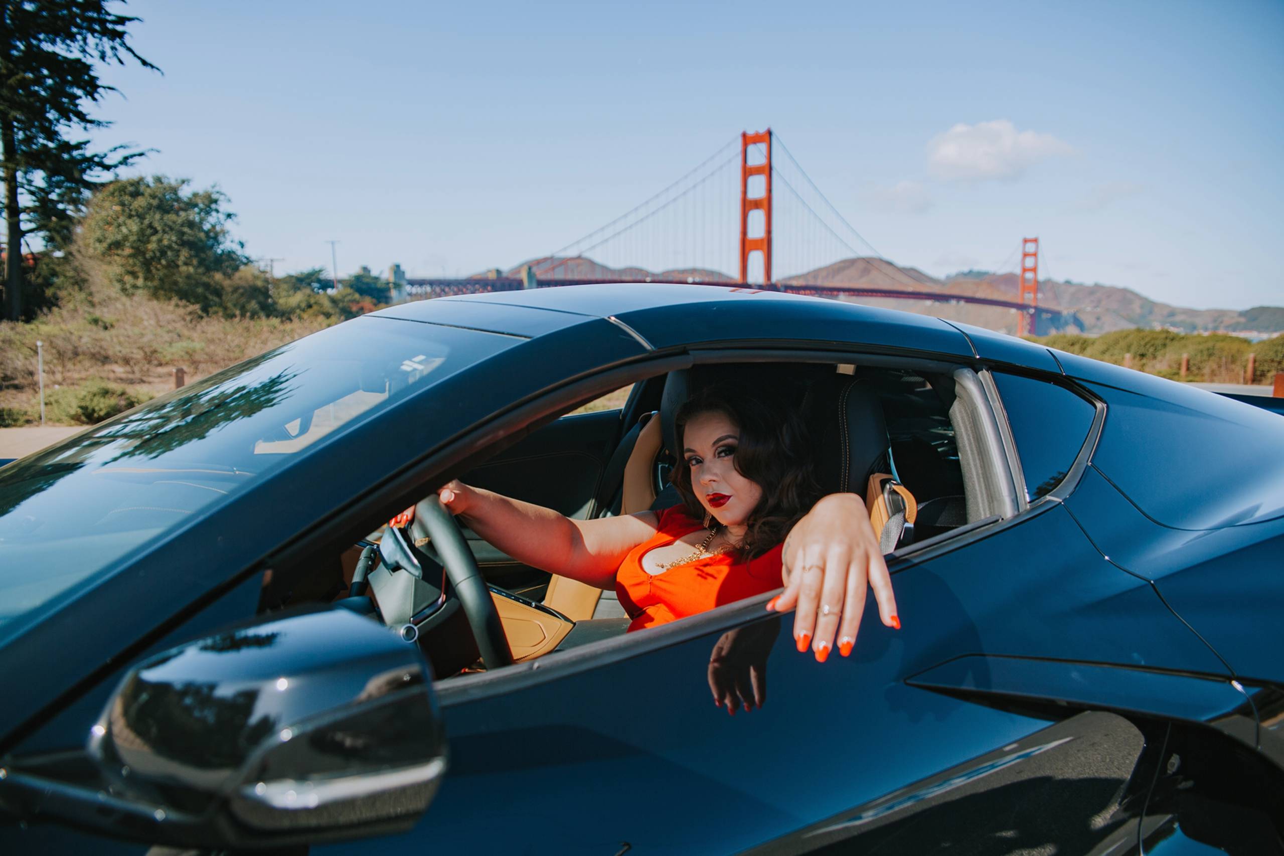 A hip-hop artist poses inside a car parked in front of the Golden Gate Bridge.