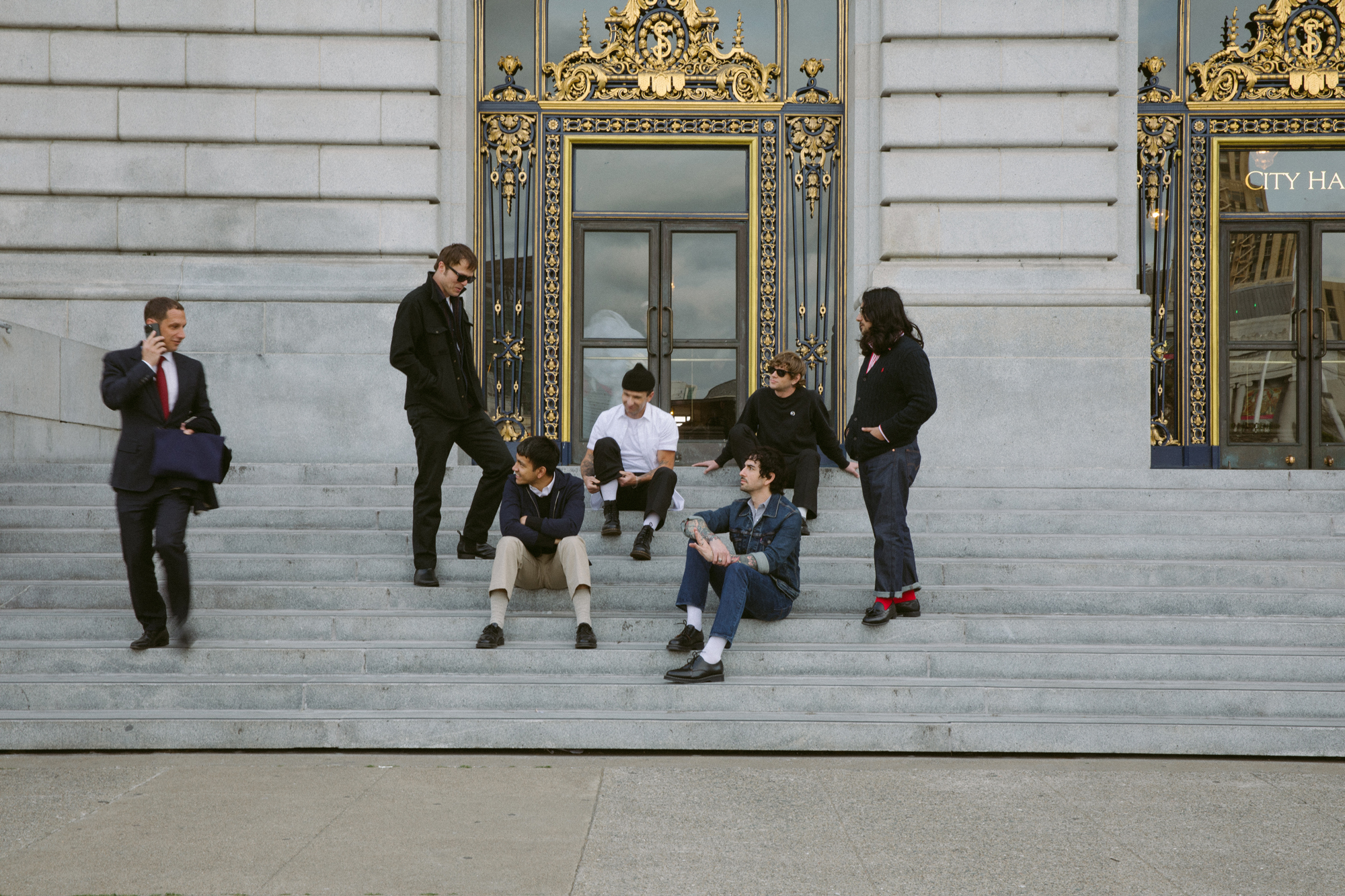 Mayor Daniel Lurie on cell phone looks at six-member band on steps