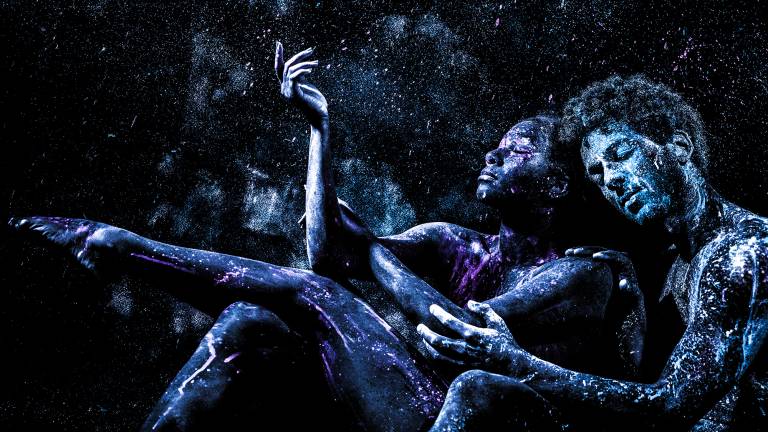 Two black- and blue-hued African American figures cradle each other against stars in the dark sky.